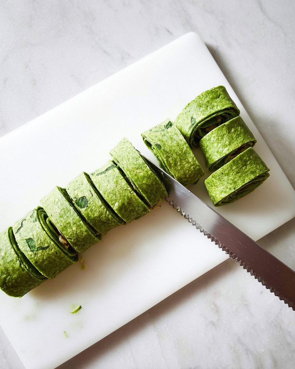 A white round plate filled with ten tightly rolled green wraps, each cut into thick slices showing three layers: a green spinach tortilla with a soft, leafy texture, a middle creamy white cheese layer, and mixed chopped spinach and small orange bits filling the center in a spiral pattern. The plate sits on a white marbled surface with a black and white striped cloth in the background, and some small pieces of dried bacon scattered around. Photo taken with an iphone --ar 4:5 --v 7