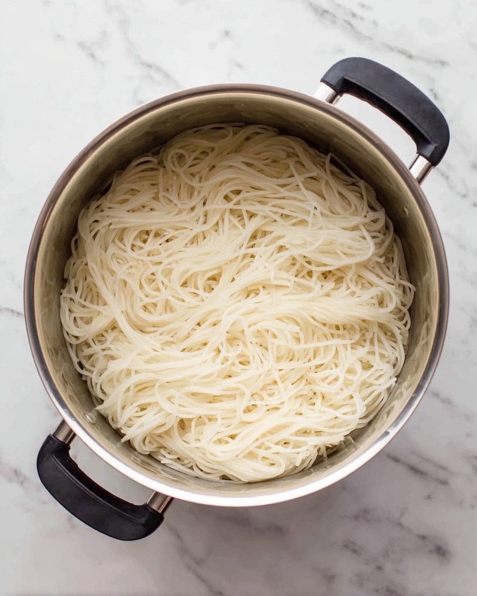 A white round bowl with ridged edges holds a colorful layered dish. At the top left, there are several thick slices of charred grilled chicken with golden brown and black edges. Below and to the left of the chicken is a pile of chopped fresh green herbs. In the center, there is a nest of smooth white rice noodles topped with crushed peanuts and a drizzle of creamy light brown sauce that covers parts of the chicken, noodles, and some of the vegetables. To the right of the noodles, thin orange carrot sticks are arranged in a small bunch. Below the carrots, there are several green cucumber pickle slices stacked and slightly overlapping. A silver fork with a wooden handle rests at the bottom center of the bowl. The bowl sits on a white marbled surface next to a striped cloth napkin. photo taken with an iphone --ar 4:5 --v 7