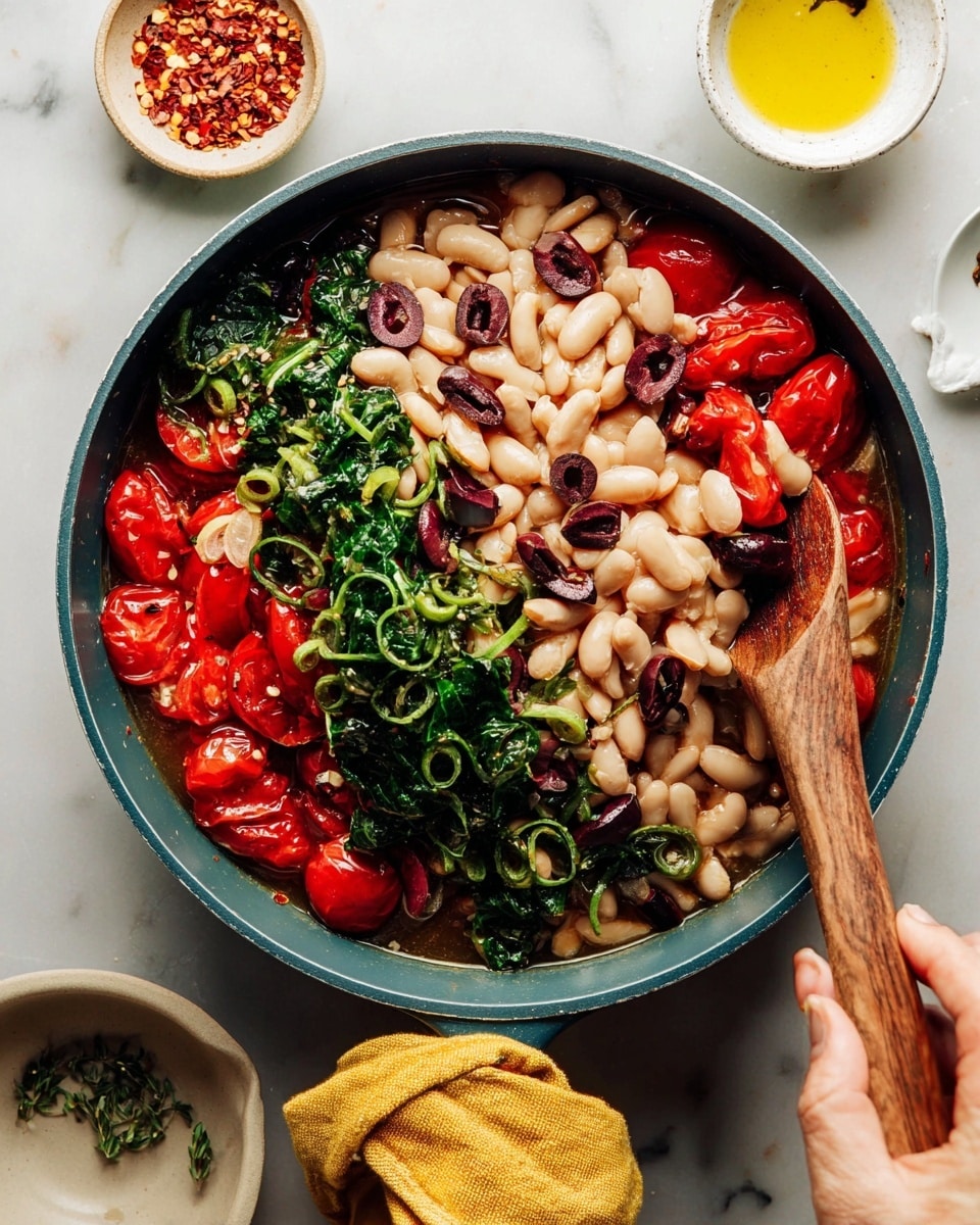 The image shows a white plate with a red rim filled with four layers of food: a base of spiral pasta in a light yellow color, scattered white beans mix in, bright red roasted cherry tomatoes placed on top, and pieces of dark purple olives and chopped dark green leafy vegetables sprinkled throughout. There is some powdered cheese spread lightly over the dish, and a silver spoon is resting on the bottom edge of the plate. The plate is set on a white marbled surface with a yellow cloth nearby, and small white bowls containing chili flakes, more cheese, olive oil, and olives are positioned around the plate. Photo taken with an iphone --ar 4:5 --v 7