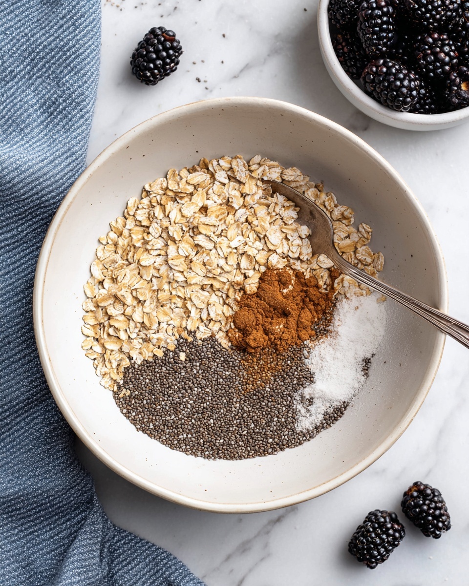 A white bowl filled with layers of ingredients including light brown oats on the upper left, small dark chia seeds covering the bottom half, a small pile of brown cinnamon powder near the center, and a white powder (likely baking soda) beside the cinnamon on the right. A silver spoon rests inside the bowl, partially buried in the chia seeds. Around the bowl, there are a few blackberries scattered on a white marbled surface, with a white bowl full of blackberries visible in the top right corner and a blue and white striped cloth in the bottom left. photo taken with an iphone --ar 4:5 --v 7