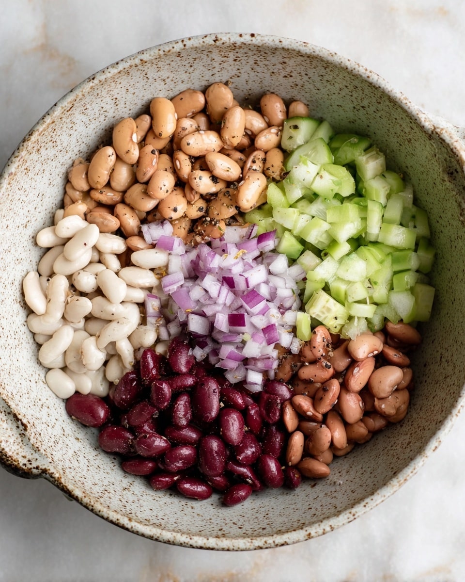 A speckled white bowl holds six sections of ingredients arranged like a colorful wheel: at the top right, light brown beans with a dark spot near one end; on the right side, diced pale green cucumber pieces; in the center, a small pile of finely chopped red onion; on the bottom right, medium brown beans; on the bottom left, dark red kidney beans; and on the left side, creamy white beans. Each ingredient looks fresh and slightly seasoned with black pepper. The bowl is set on a white marbled surface. photo taken with an iphone --ar 4:5 --v 7